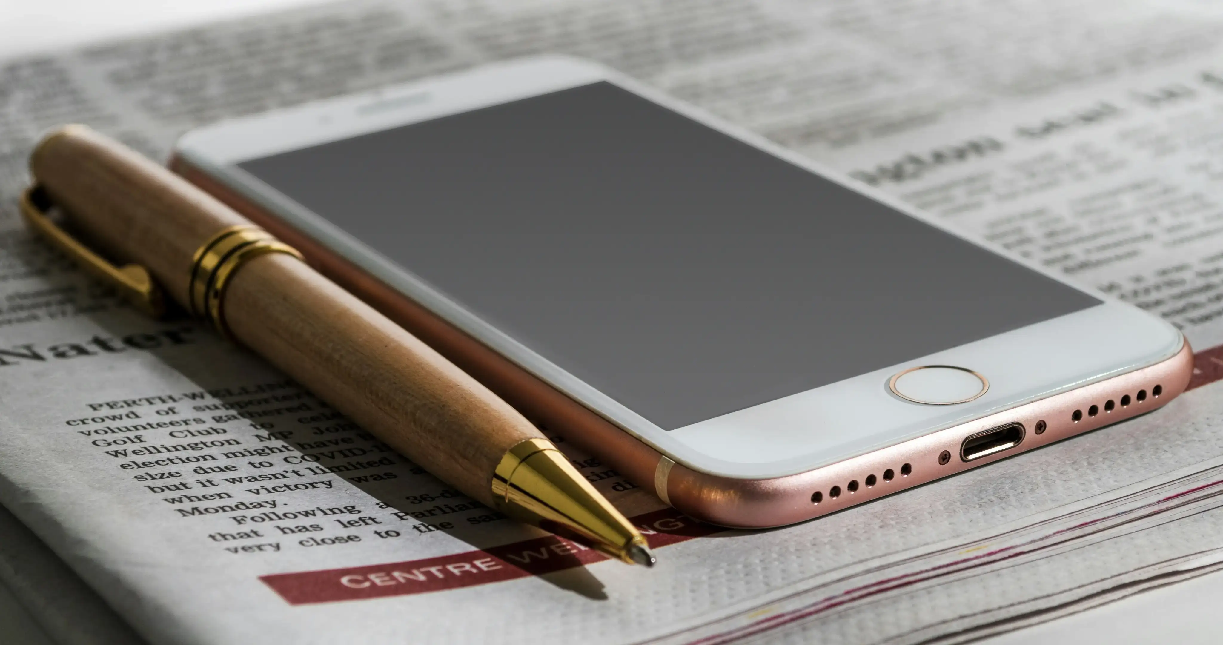 Ein Handy und ein Kugelschreiber auf einer Zeitung sollen eine Nachrichtenübersicht darstellen.